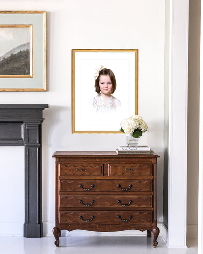 Wooden dresser with a custom framed heirloom portrait and flowers against a white wall.